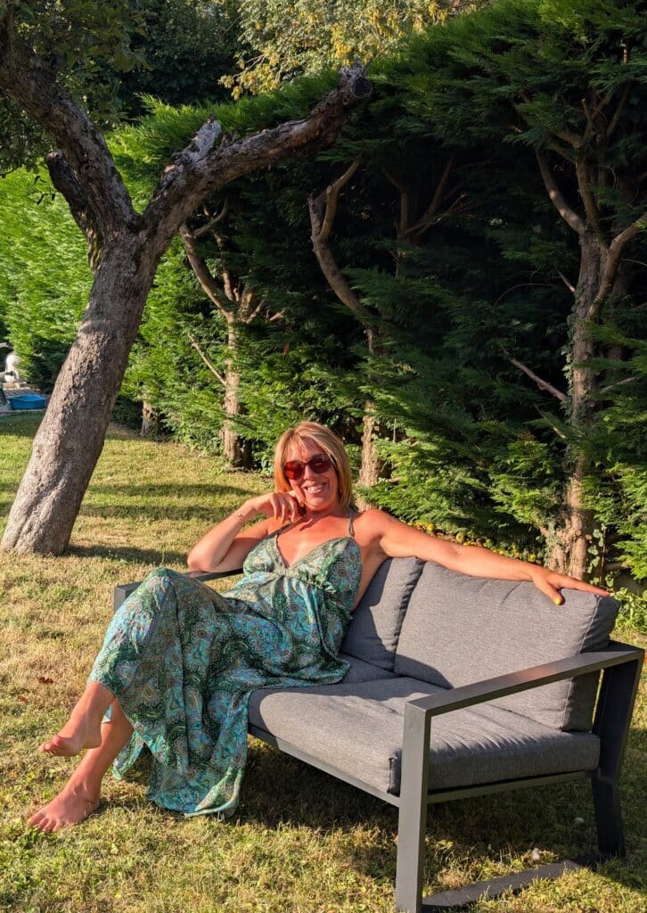 Céline, coach en nutrition générale et spécialisée pour femmes en pré-ménopause et ménopause, assise dans son jardin, souriante devant un fond naturel.