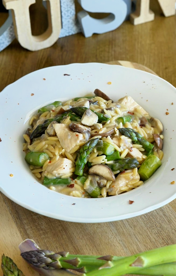 Orzo crémeux aux asperges avec une sauce onctueuse, parsemé d’asperges vertes et servi chaud dans une assiette élégante