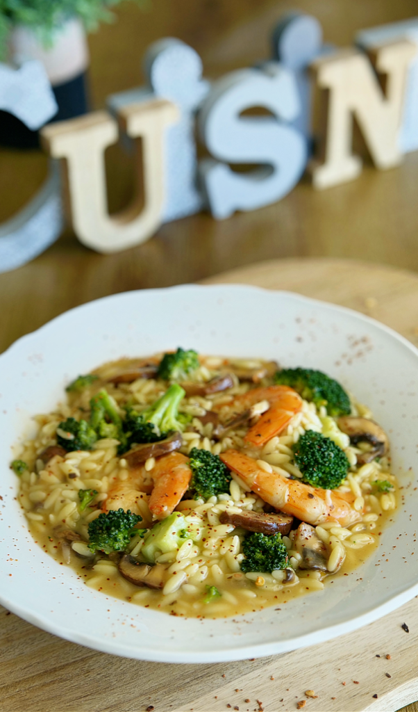 Orzo crémeux aux crevettes avec une sauce onctueuse, parsemé d’herbes fraîches et servi chaud dans une assiette élégante