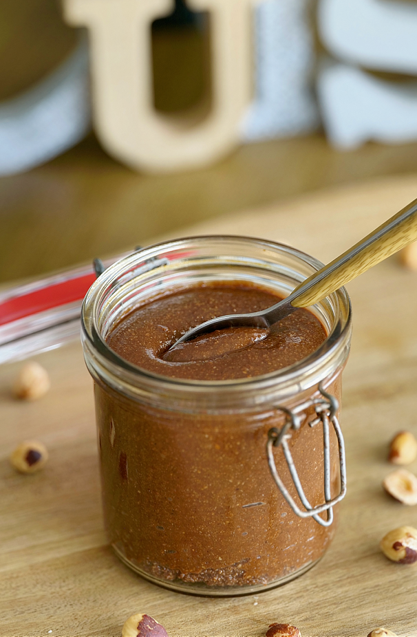 Pâte à tartiner choco-noisette maison onctueuse dans un pot avec des noisettes entières et du chocolat