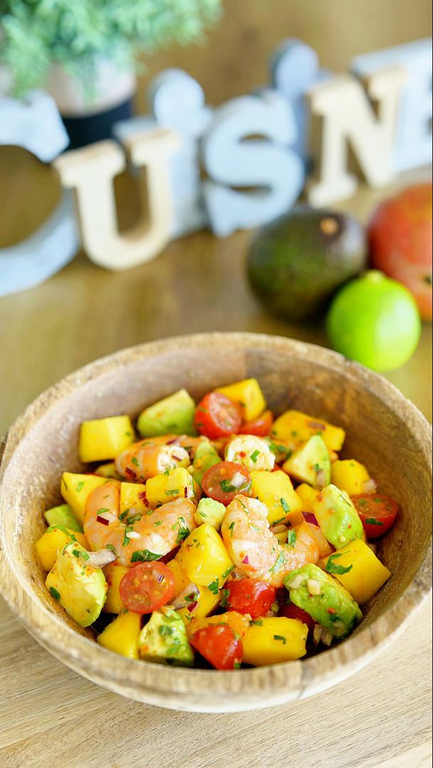 Salade de crevettes, mangue et avocat dans une assiette fraîche et colorée, composée de crevettes, morceaux de mangue, avocat, légumes et herbes fraîches, idéale pour un repas léger et équilibré.