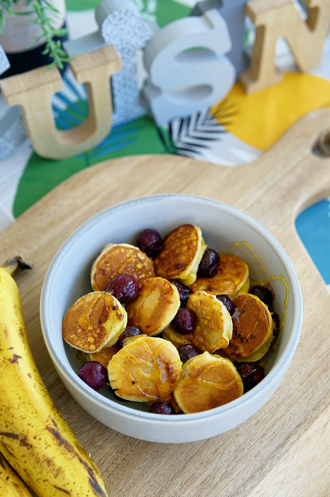 Mini pancakes cœur de banane moelleux servis avec des rondelles de banane et une garniture gourmande, parfaits pour un petit-déjeuner sain et équilibré.